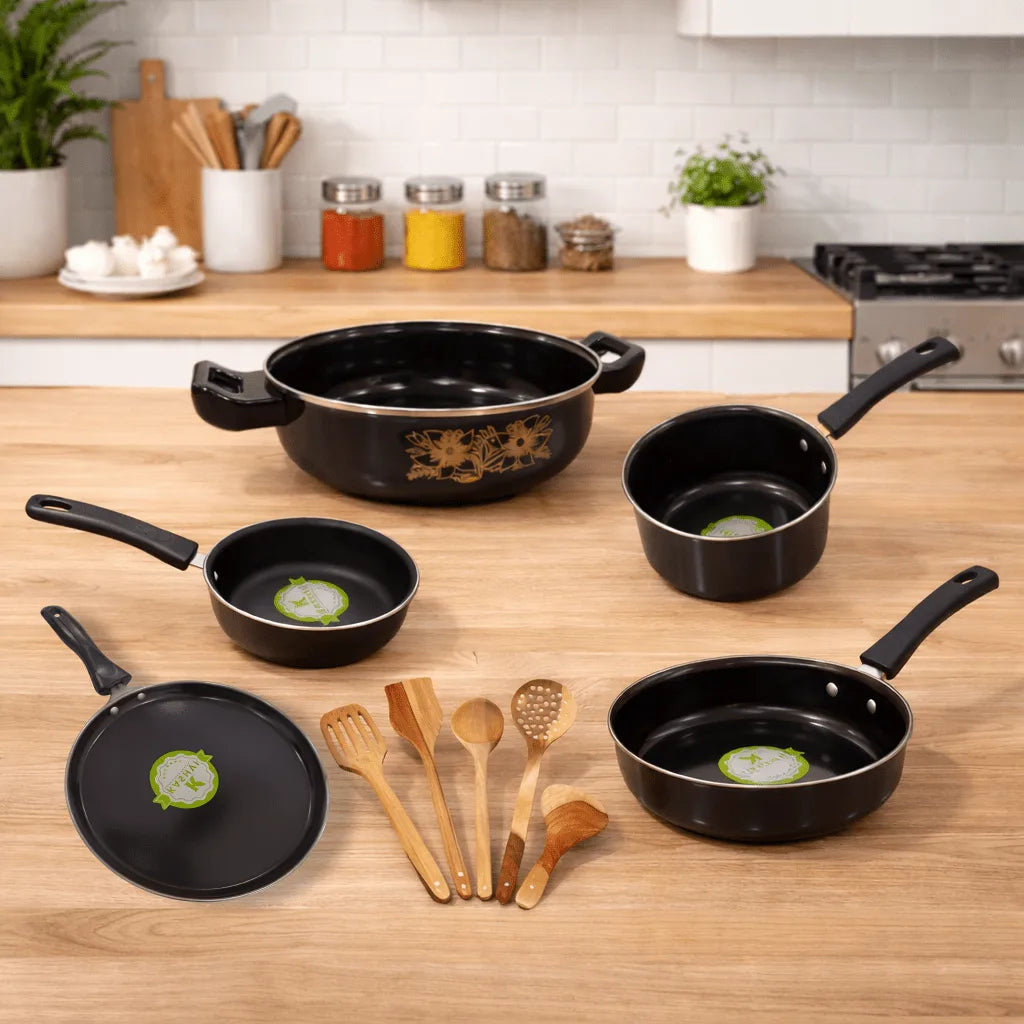 Set of black cookware on a wooden kitchen counter with wooden utensils.