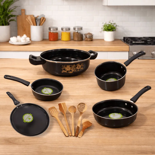 Set of black cookware on a wooden kitchen counter with wooden utensils.