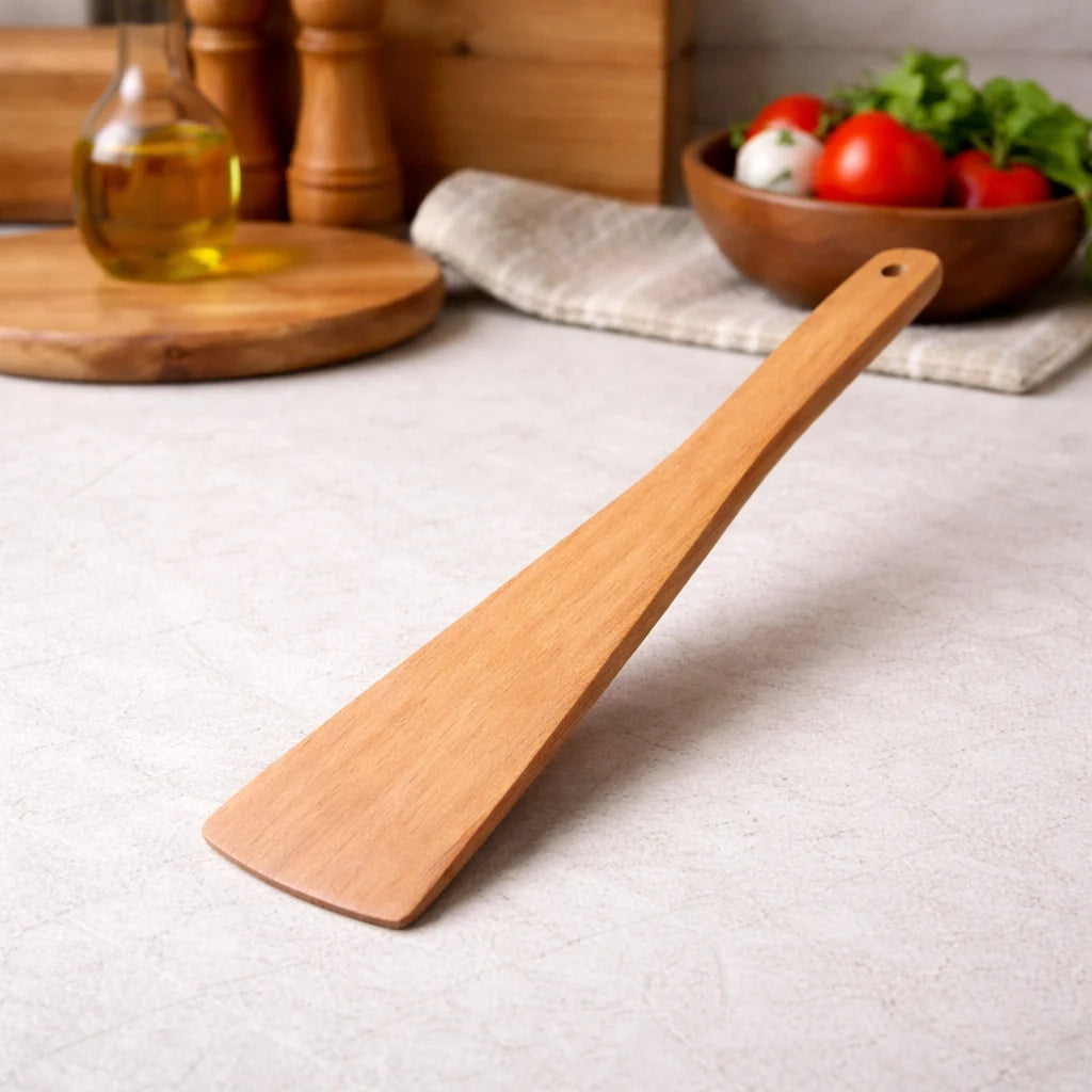 Wooden spatula on a kitchen counter with a bowl of vegetables in the background