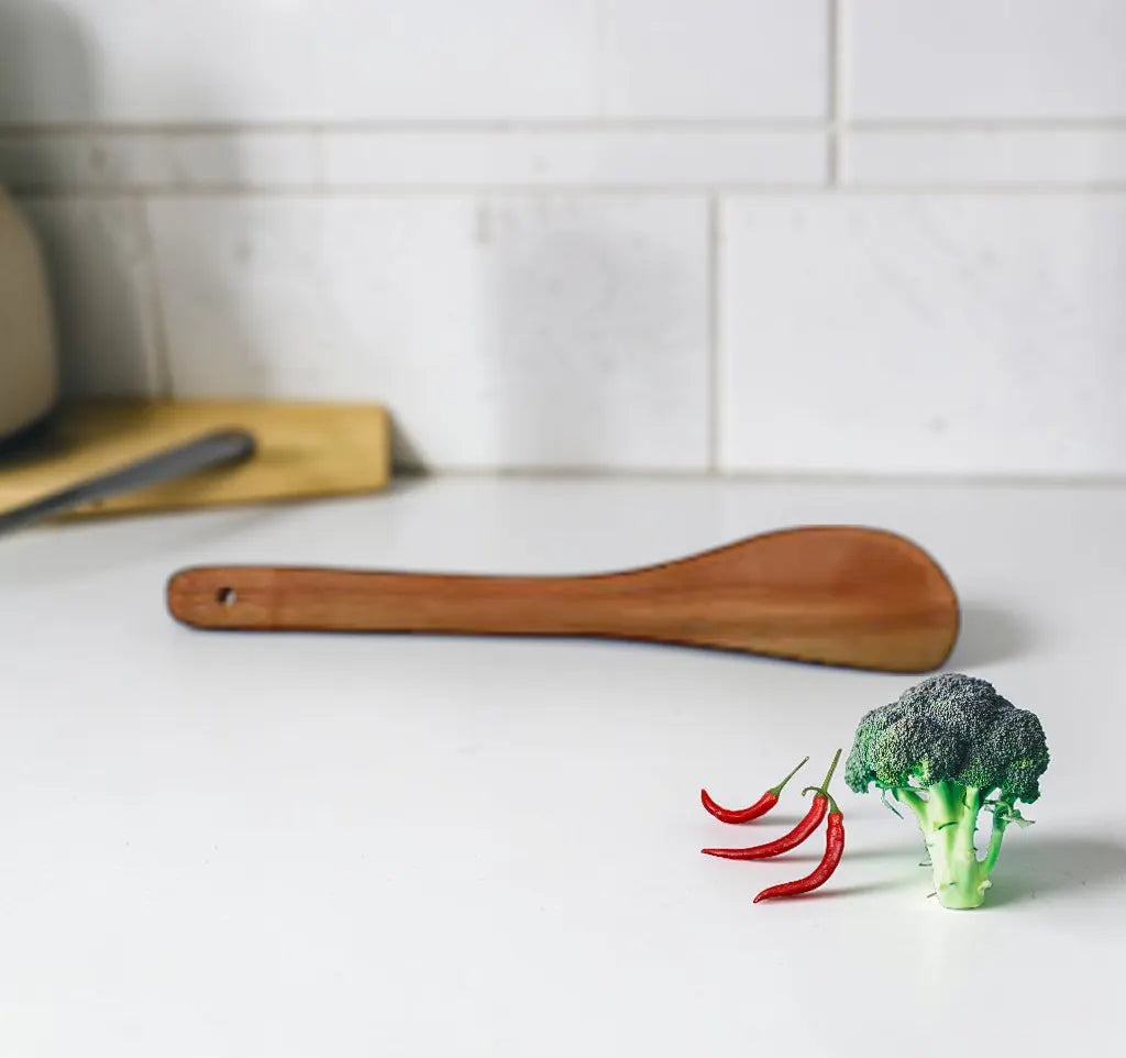 Broccoli and red chilies on a white surface with a wooden spatula in the background.