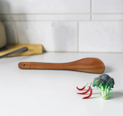 Broccoli and red chilies on a white surface with a wooden spatula in the background.