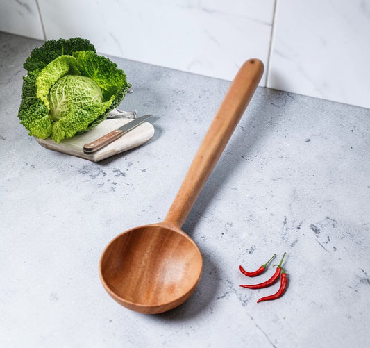 Wooden ladle on a gray surface with a head of cabbage, knife, and red peppers.