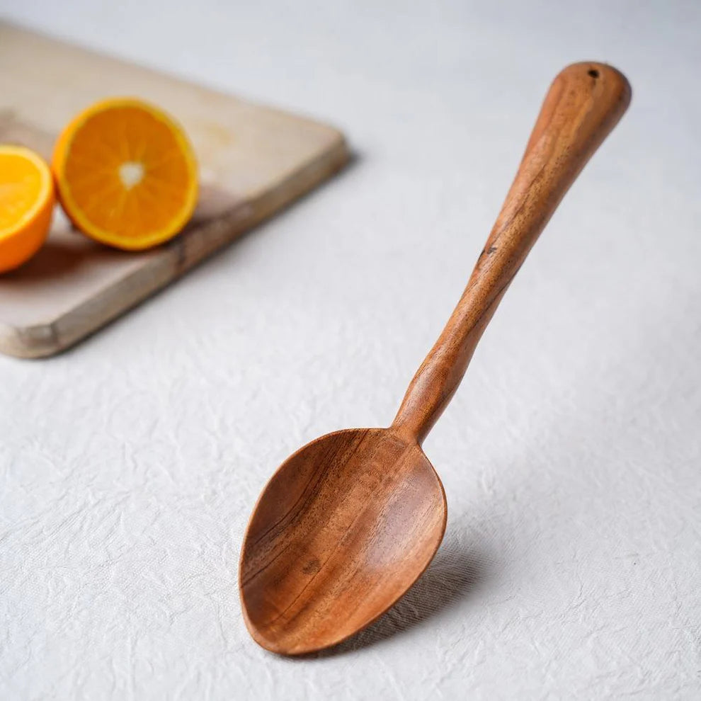 Wooden spoon on a light surface with oranges in the background
